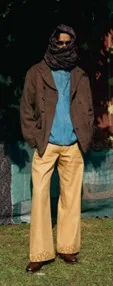 Full-length layered outfit with oversized coat, wrapped scarf, and wide-leg trousers outdoors, illustrating protective, shape-easy styling