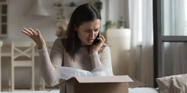 Frustrated woman opening a delivery box while on the phone, illustrating online order disappointment