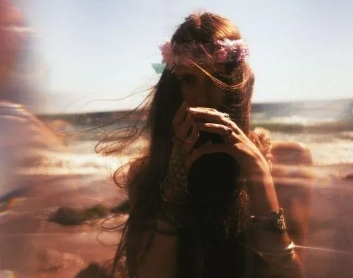 Woman on a beach at golden hour with flower crown and layered jewellery, evoking a boho aesthetic