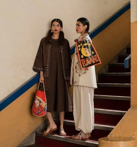 Two women on a staircase in tailored ethnic-inspired co-ords with embroidery and graphic totes, timeless silhouettes with modern personality