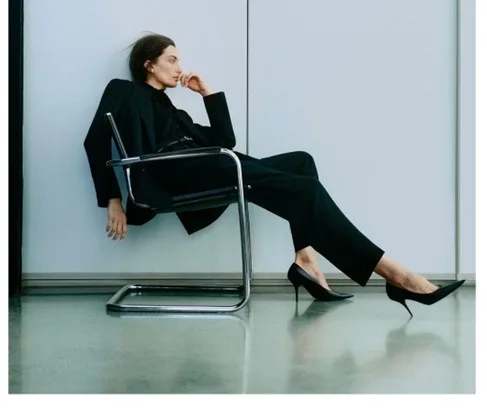 Woman in a black tailored suit and heels seated in a minimalist office, polished corporate first-day look