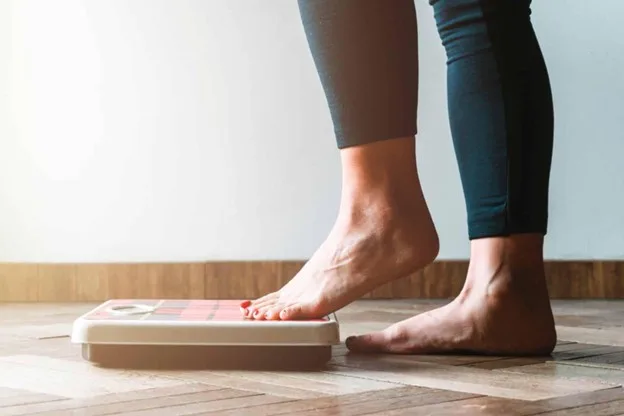 Person stepping onto a scale, representing weight change and the start of a wardrobe transition
